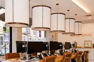 Carter-Jonas White drum lampshades with bronze metal detail shown in a row above a desk of computer screens