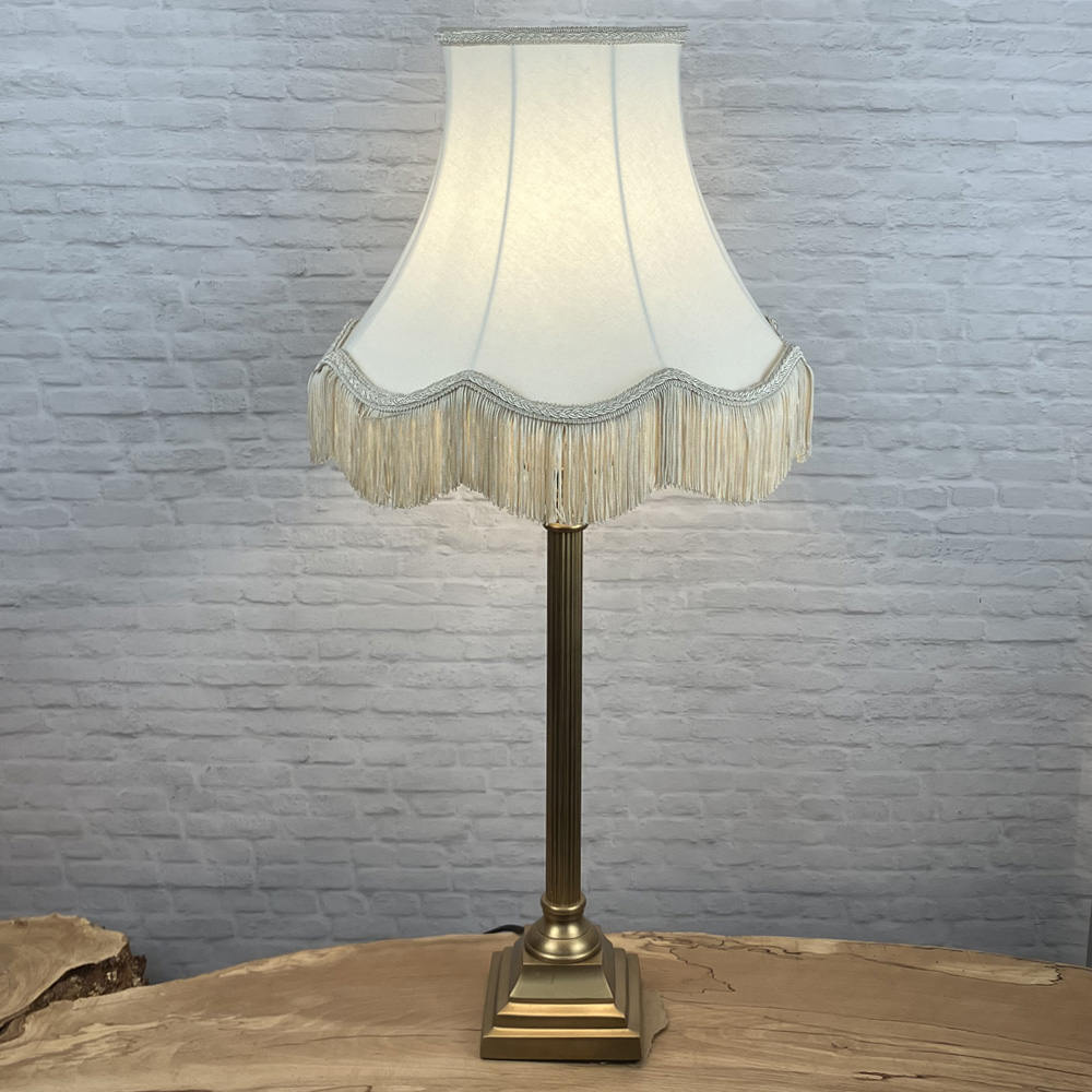 Scalloped bowed empire lampshade in cream with a dark cream fringe on a table lamp