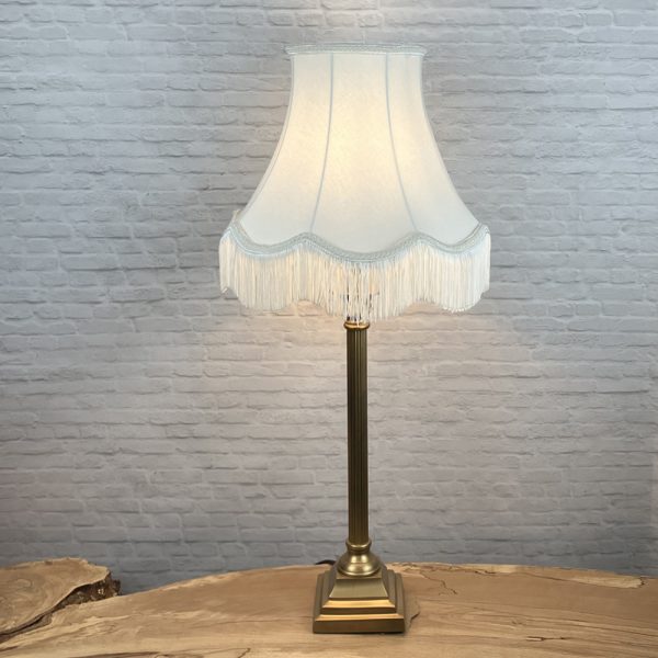 Off white scalloped bowed empire lampshade with matching natural fringe shown on a table lamp