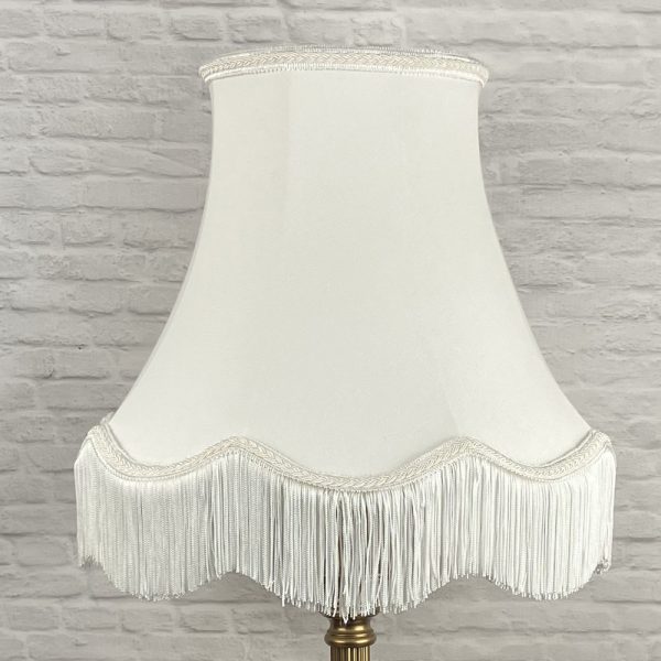 Off white scalloped bowed empire lampshade with matching natural fringe shown on a table lamp