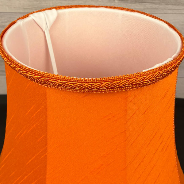 Close up image of the Retro Bright Orange Faux Silk Lampshade with a Matching Plait Trim. Showing the soft white internal lining.