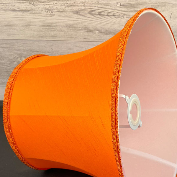 Close up image of a Traditional Bright Orange Faux Silk Lampshade with a matching Plait Trim, showing the inside soft white lining