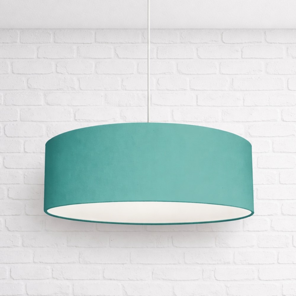Teal drum pendant lampshade hanging from white ceiling against white brick wall