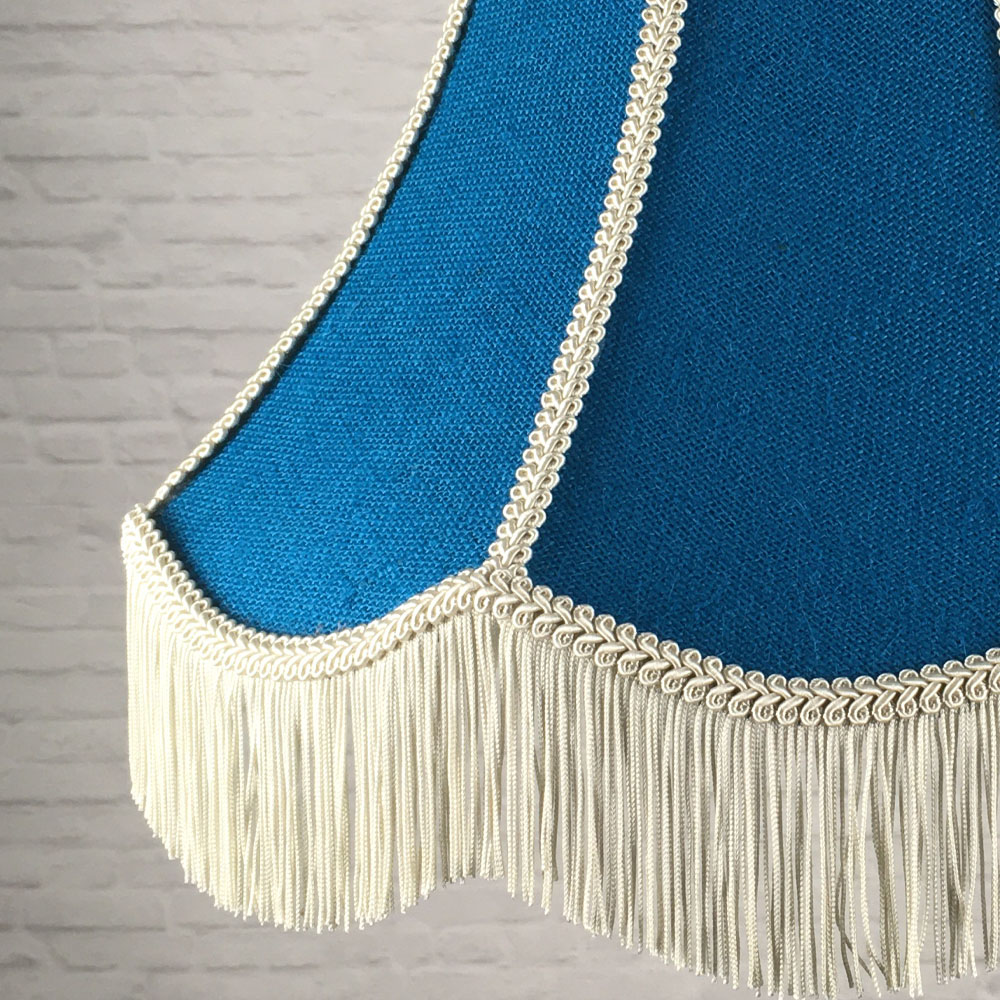 Close-up of blue hessian lampshade with dark cream trim and cream fringe detail