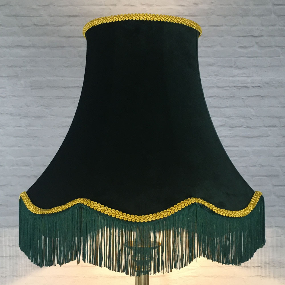 Dark green velvet scalloped bowed empire lampshade illuminated on a table lamp, highlighting the decorative yellow feather trim, coordinating green fringe, and warm gold lining while creating a rich ambient glow