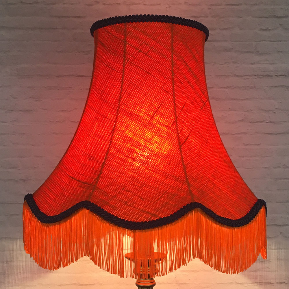 Illuminated orange hessian scalloped bowed empire lampshade with navy trim and fringe on table lamp