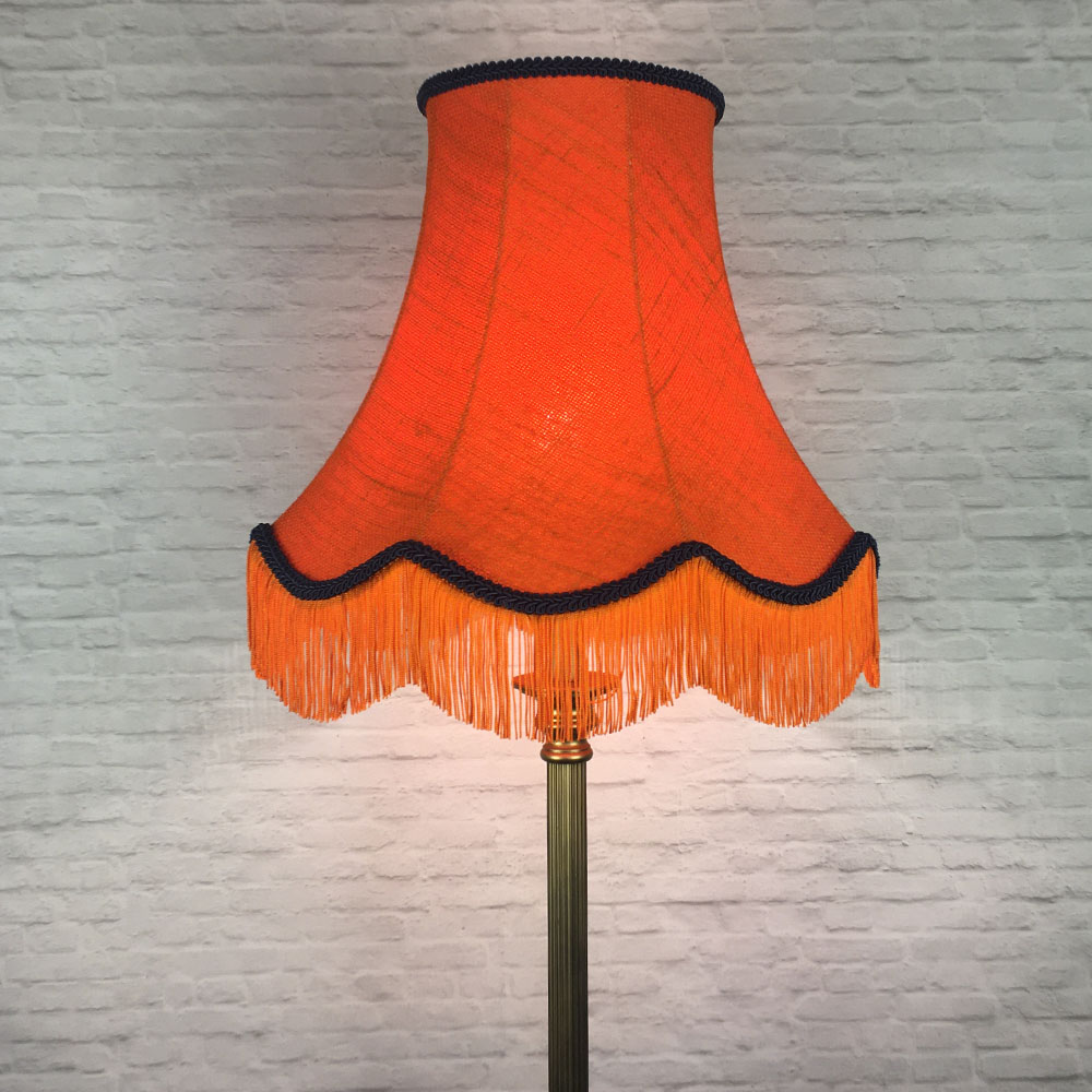 Illuminated orange hessian scalloped bowed empire lampshade with navy trim and fringe on floor lamp