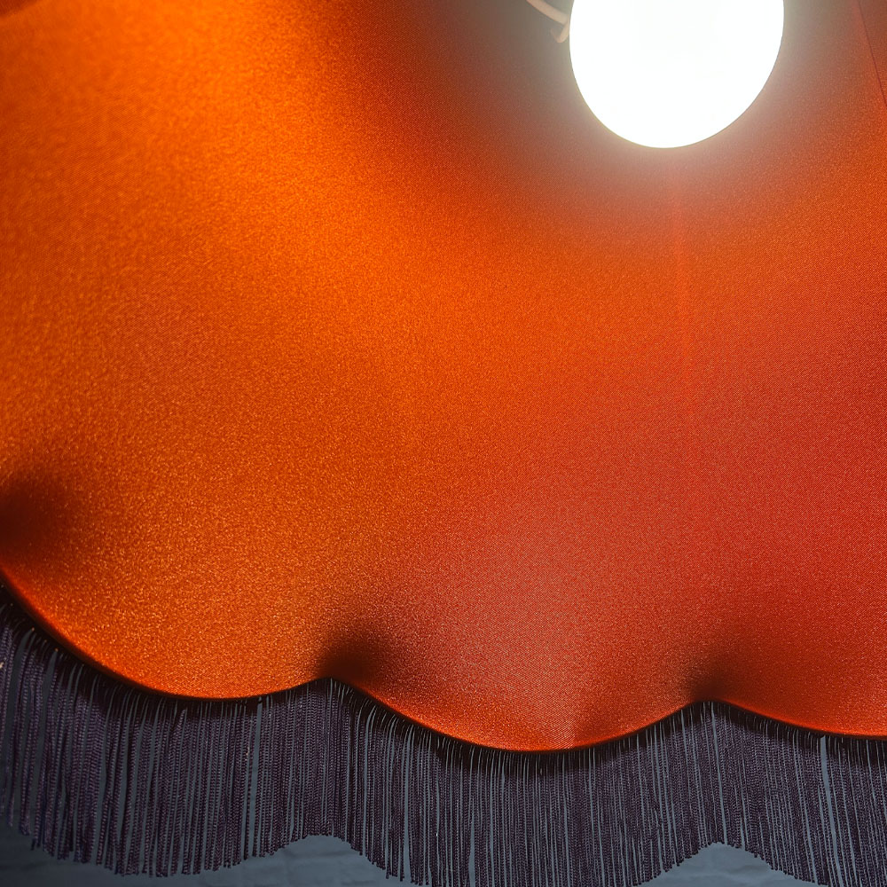 Close-up of orange lining inside navy velvet scalloped bowed empire lampshade
