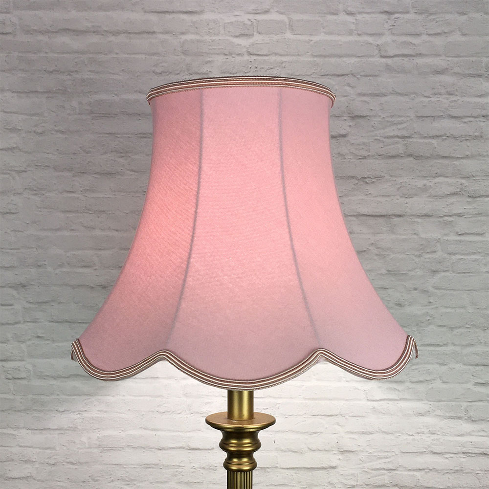 Illuminated pale pink scalloped bowed empire lampshade on antique brass standing lamp