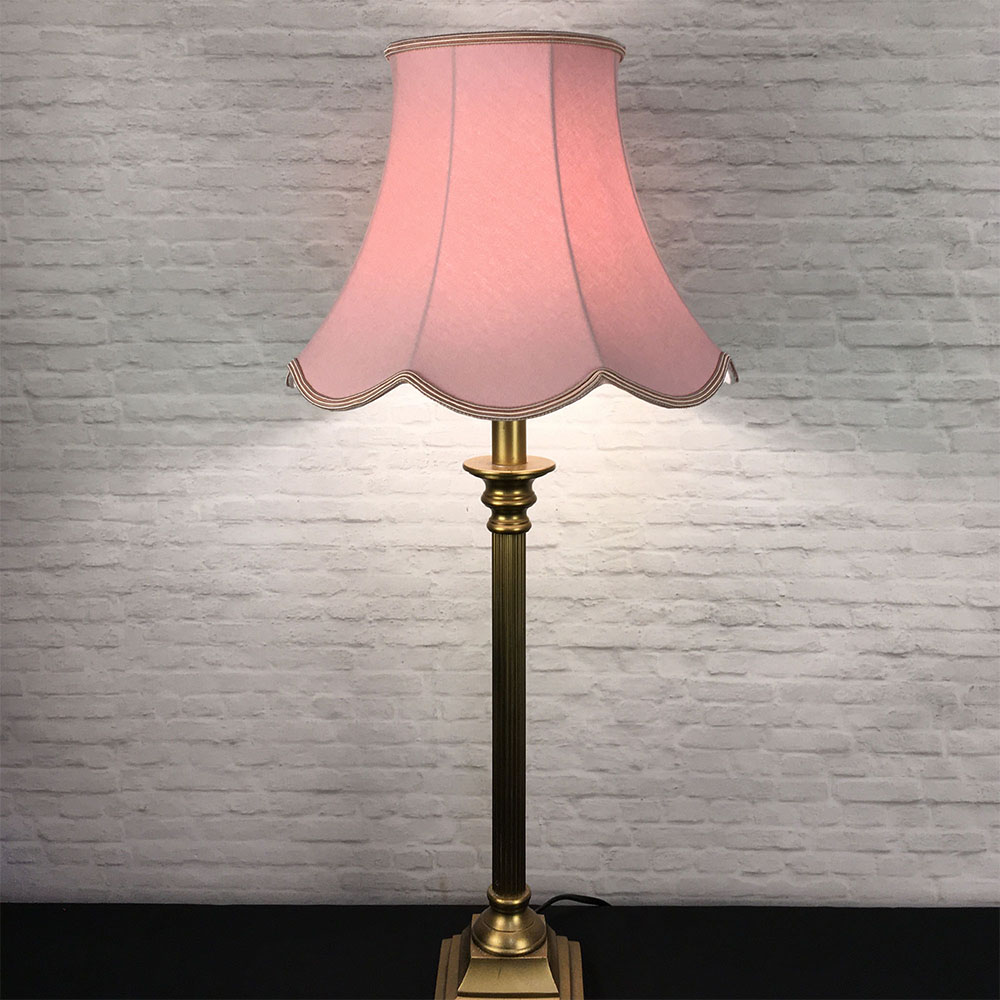 Illuminated pale pink scalloped bowed empire lampshade on antique brass table lamp