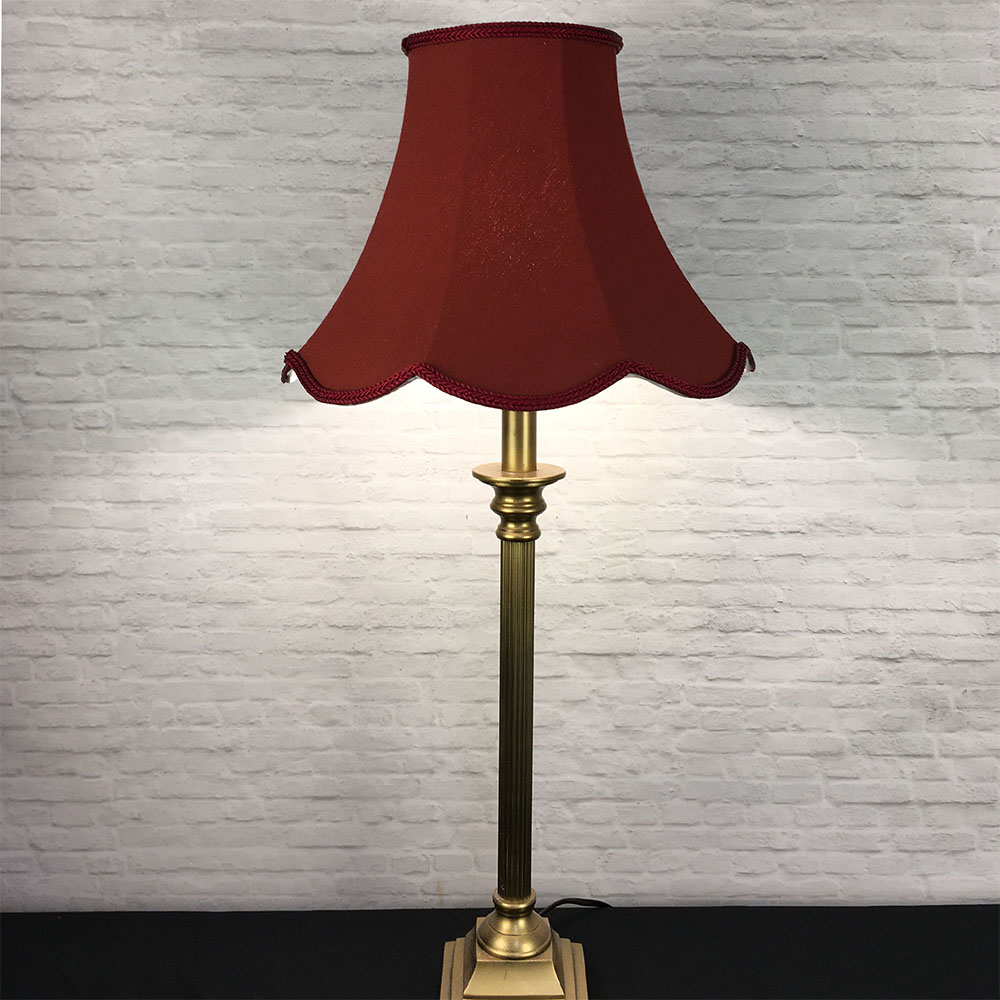 Illuminated ruby scalloped bowed empire lampshade on antique brass table lamp