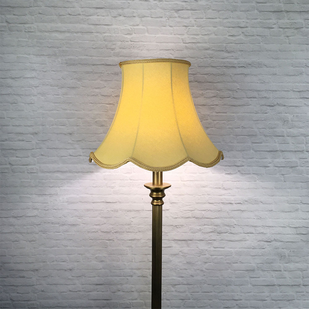 Illuminated soft gold scalloped bowed empire lampshade on antique brass standing lamp