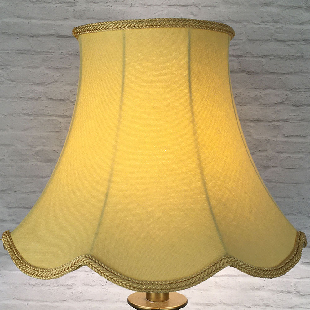 Illuminated soft gold scalloped bowed empire lampshade on antique brass standing lamp