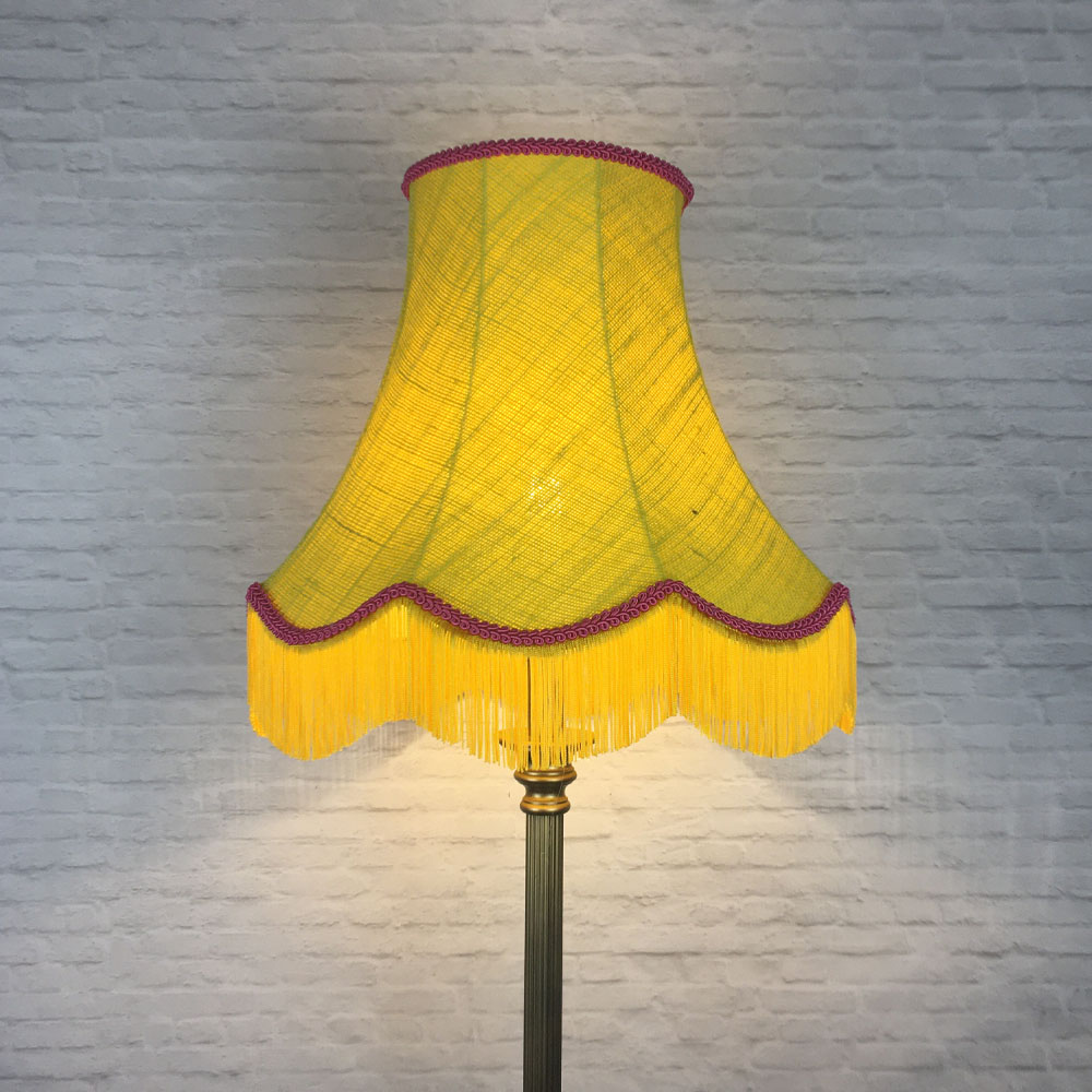 Illuminated yellow hessian scalloped bowed empire lampshade with pink trim and pink fringe on table lamp